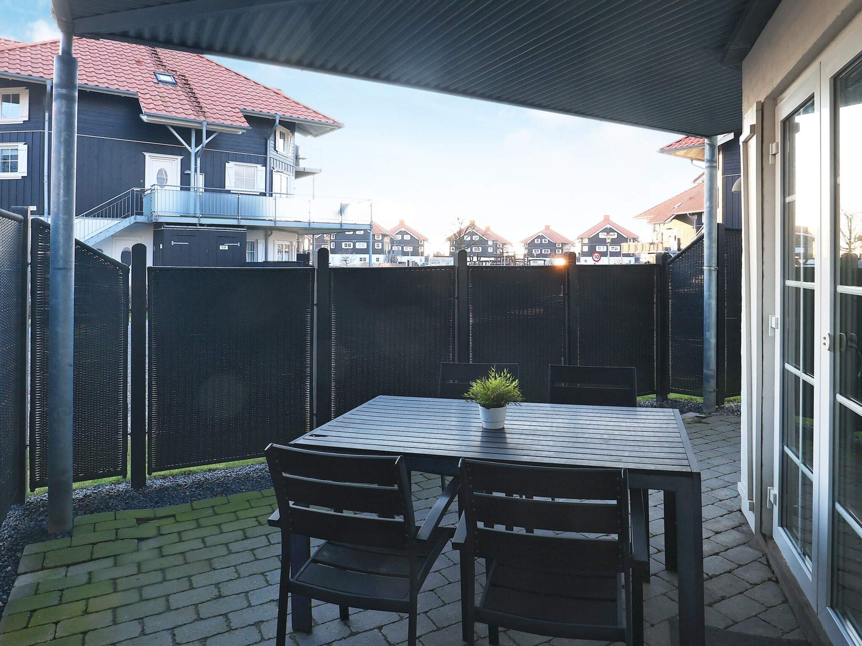 Eine Terrasse im Freien mit Tisch und Stühlen, einem Blumentopf und Blick auf angrenzende Häuser.