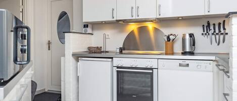 Een kleine keuken met witte kasten, een inbouwoven en een koffiezetapparaat.