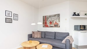 A modern living room with a grey sofa, two wooden side tables, a hanging light fixture, and a wall-mounted artwork of Paris. - 5 Person Holiday Home in Bogense (Bogense)