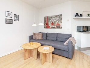 A modern living room with a grey sofa, two wooden side tables, a hanging light fixture, and a wall-mounted artwork of Paris. - 5 Person Holiday Home in Bogense (Bogense)