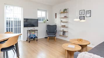 Ein modernes Wohnzimmer mit einem Flachbildfernseher, einem grauen Sessel, einem Holzesstisch und einem runden Couchtisch.