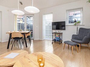 Ein modernes Wohnzimmer mit Essbereich, einem Flachbildfernseher an der Wand und einem grauen Sessel.