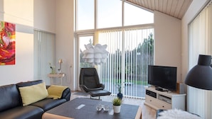 A modern living room with a black leather sofa, a coffee table, a TV, and a large window with blinds. - 6 Person Holiday Home in Vaeggerlose (Vaeggerlose)