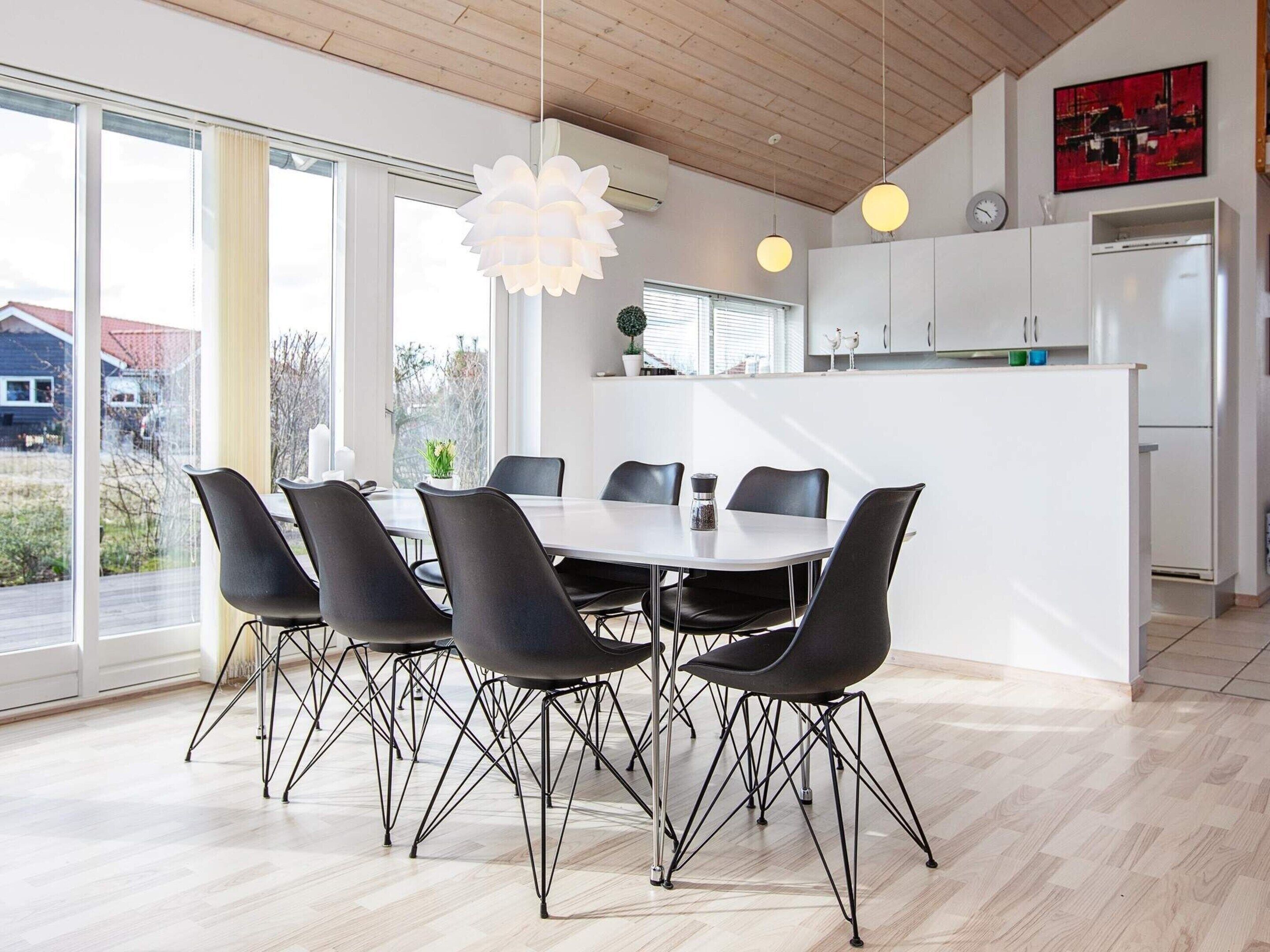 A modern kitchen with a white island, black chairs, and pendant lights.