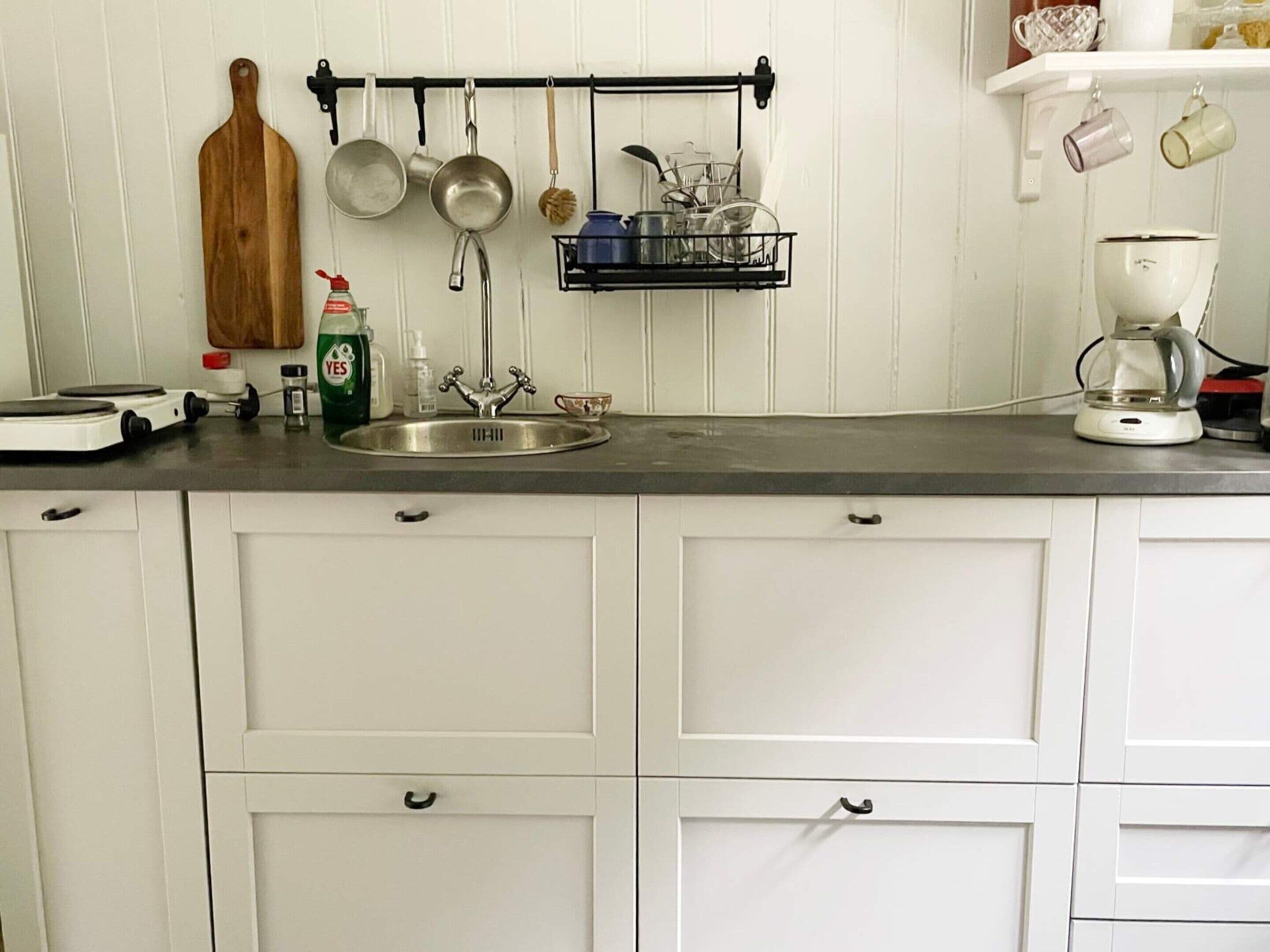 A kitchen with a stainless steel sink, white cabinets, a hanging pot rack, and a coffee maker.