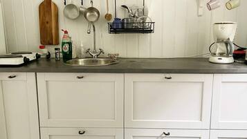 A kitchen with a stainless steel sink, white cabinets, a hanging pot rack, and a coffee maker.