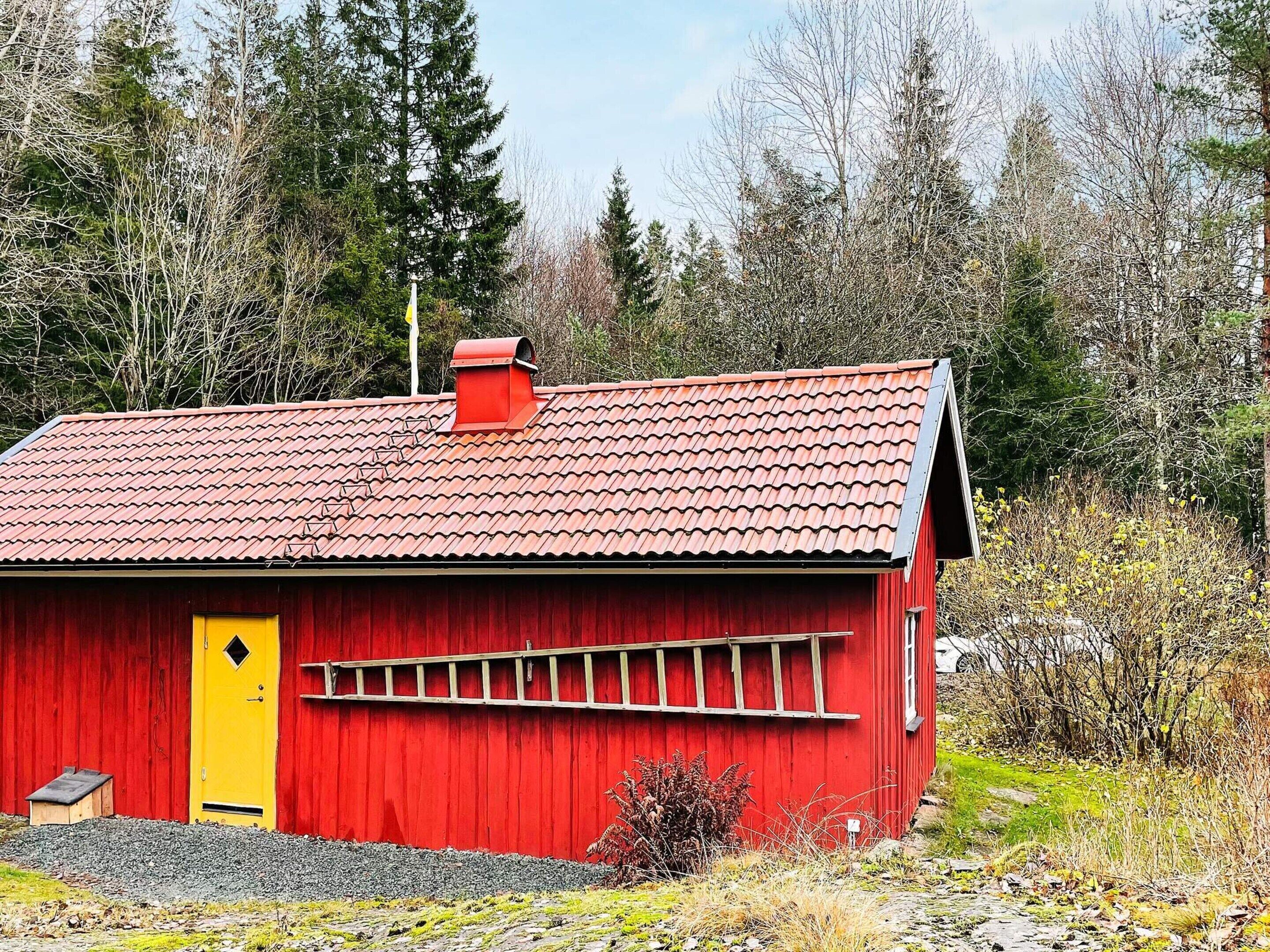 A red wooden building with a yellow door, a red roof, and a small chimney.