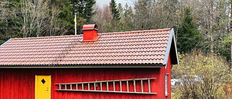 A red wooden building with a yellow door, a red roof, and a small chimney.