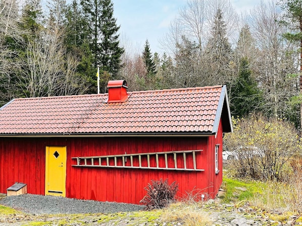 A red wooden building with a yellow door, a red roof, and a small chimney.