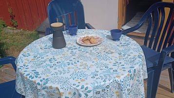 A round table with a floral tablecloth, two blue chairs, a plate of cookies, a blue mug, and a gray pitcher.