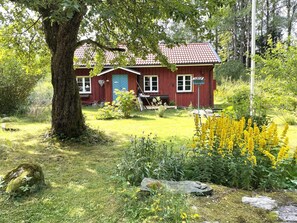 A red wooden house with a tiled roof, surrounded by a grassy yard and various plants. - 3 Person Holiday Home in Uddevalla (Uddevalla)