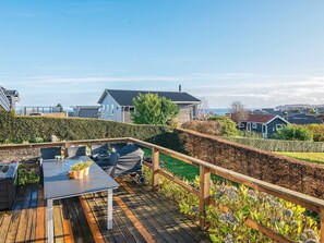 Une terrasse en bois avec une table et des chaises, entourée d’une clôture en bois et de parterres de fleurs.