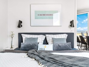 A modern bedroom with a large bed, a framed quote on the wall, and a view of the outdoors. - 5 Star Holiday Home in Wendtorf (Wendtorf)