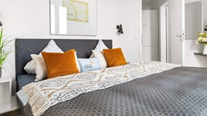 A modern bedroom with a bed, pillows, a bedside table, a lamp, and a framed picture on the wall.