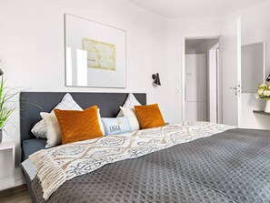 A modern bedroom with a bed, pillows, a bedside table, a lamp, and a framed picture on the wall.