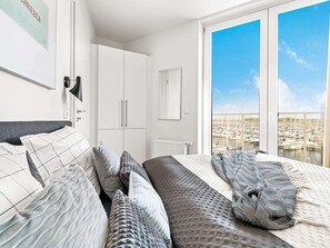 A bedroom with a bed, a wardrobe, a radiator, and a view of a marina through large windows. - 5 Star Holiday Home in Wendtorf (Wendtorf)