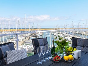 A balcony with a table set for two, overlooking a marina with numerous boats. - 5 Star Holiday Home in Wendtorf (Wendtorf)