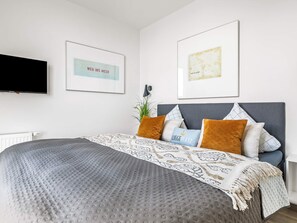 A modern bedroom with a large bed, a flat-screen TV, and two framed artworks on the wall. - 5 Star Holiday Home in Wendtorf (Wendtorf)
