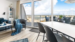 A modern living room with a balcony overlooking a beach and marina.
