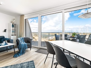 A modern living room with a balcony overlooking a beach and marina.