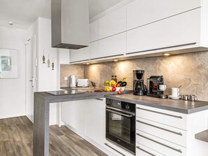 A modern kitchen with white cabinetry, a built-in oven, and a coffee station. - 5 Star Holiday Home in Wendtorf (Wendtorf)