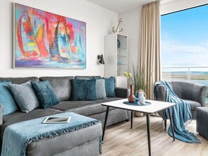 Ett modernt vardagsrum med en grå soffa, ett soffbord och utsikt över havet.