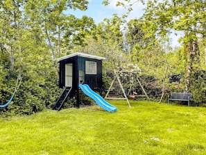 A playhouse with a slide and a swing set in a grassy area surrounded by trees. - 5 Star Holiday Home in Graested (Graested)