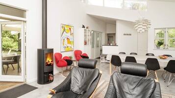 Un interior moderno con chimenea, zona de estar, comedor y vistas al exterior.
