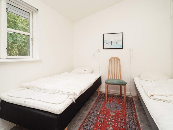 A small, clean room with two beds, a chair, a rug, and a window with greenery outside.