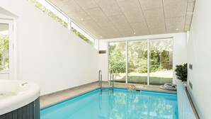 Piscina interna com hidromassagem, grandes janelas e vista para o verde lá fora.