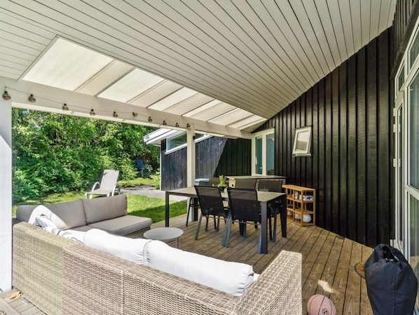 A covered outdoor area with a sofa, dining table, and chairs. - 5 Star Holiday Home in Graested (Graested)