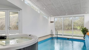 Una piscina interior moderna con un jacuzzi, ventanas amplias y vistas al exterior.