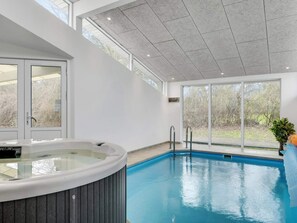 En modern inomhuspool med bubbelbad, stora fönster och utsikt över omgivningen.