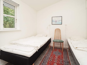 A small, tidy room with two single beds, a chair, a rug, and a window with a view of trees.