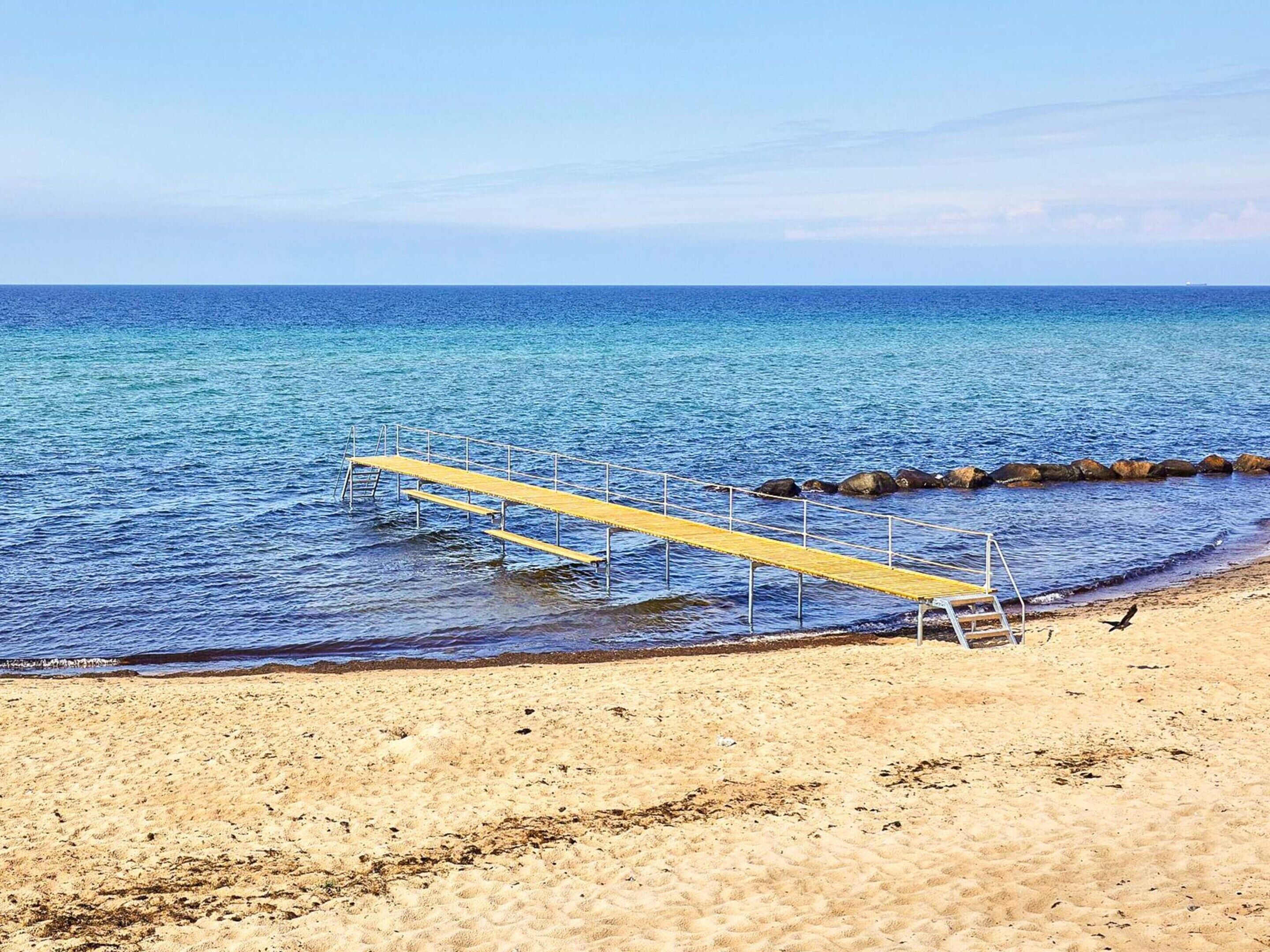 A beach with a wooden pier extending into the sea, surrounded by rocks and sandy shore.