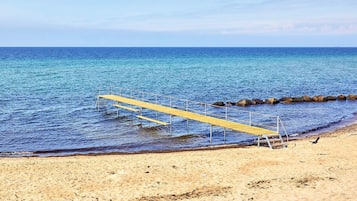 A beach with a wooden pier extending into the sea, surrounded by rocks and sandy shore.