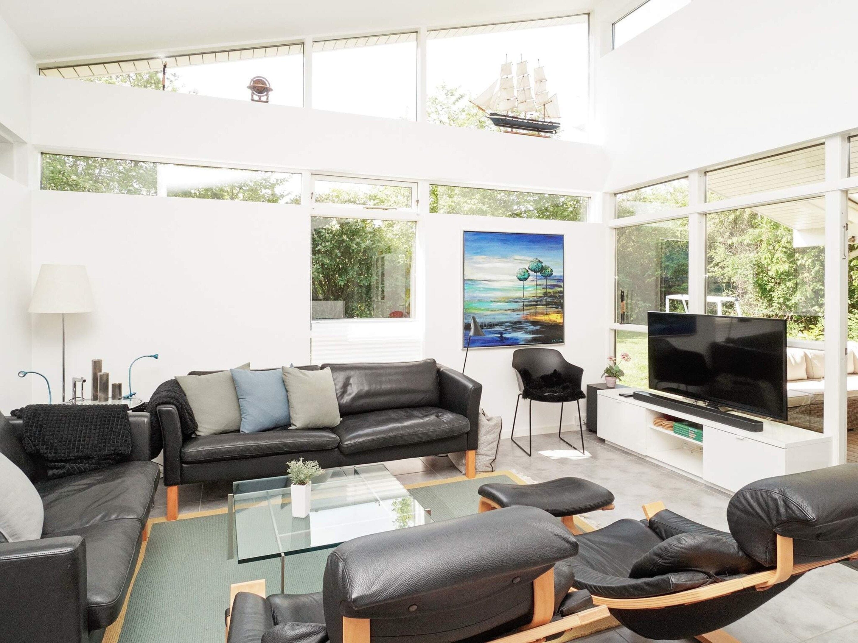 Een moderne woonkamer met een zwarte leren bank, een glazen salontafel en een flatscreen televisie.