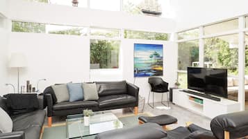 Een moderne woonkamer met een zwarte leren bank, een glazen salontafel en een flatscreen televisie.