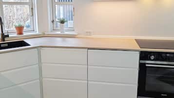 A modern kitchen with white cabinetry, a built-in oven, and a window with a potted plant.