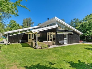 A modern house with a covered patio, a visible deck, and a well-maintained lawn. - 5 Star Holiday Home in Graested (Graested)