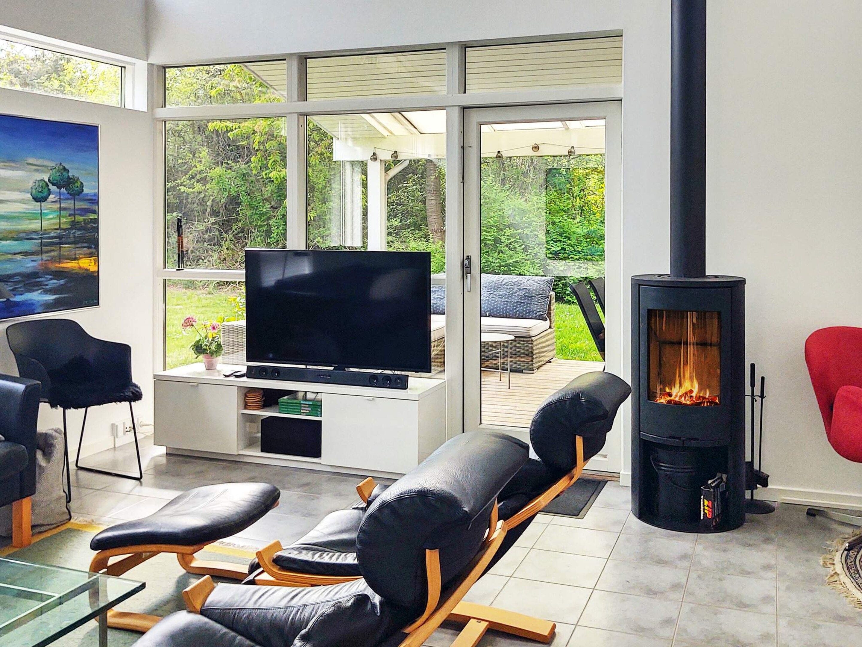 Ein modernes Wohnzimmer mit Flachbildfernseher, Ledersofas, einem Glastisch und einem Kaminofen.