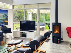A modern living room with a flat-screen TV, leather sofas, a glass coffee table, and a wood-burning stove. - 5 Star Holiday Home in Graested (Graested)