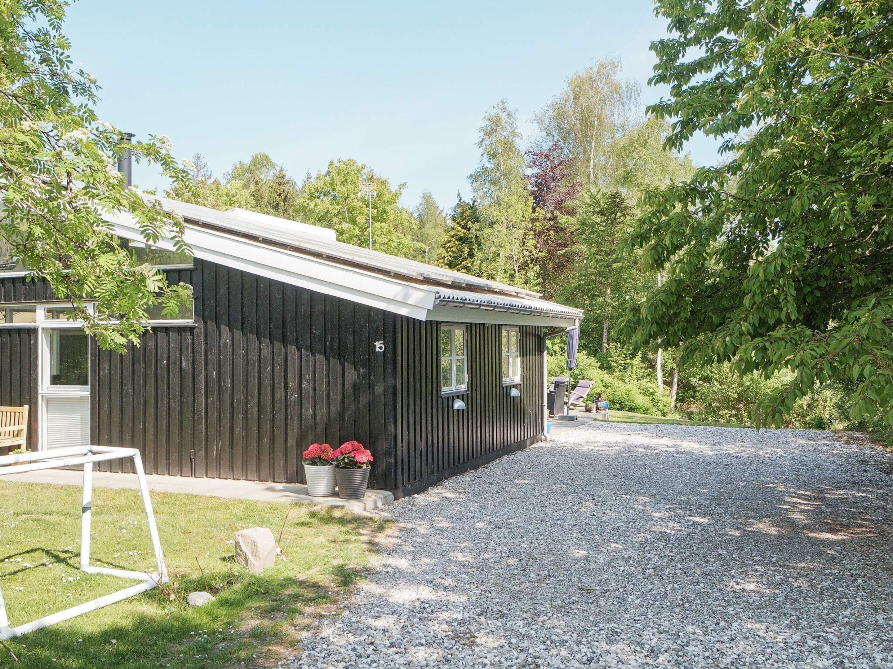 A single-story building with a dark exterior, a gravel driveway, and a small garden area with potted plants.