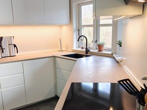 A modern kitchen with white cabinetry, a black countertop, a window with a view, and a built-in stove.