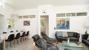 Uma sala de estar moderna com área de refeições, apresentando um sofá, cadeiras, mesa de centro e obras de arte nas paredes.