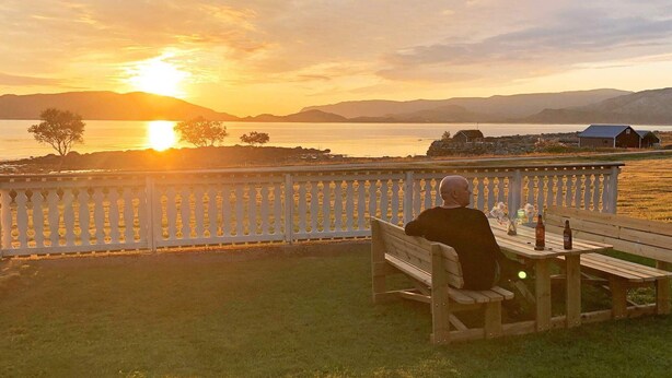 A person sitting on a bench overlooking a sunset over a body of water with distant mountains. - 4 Star Holiday Home in Svelgen (Bremanger)