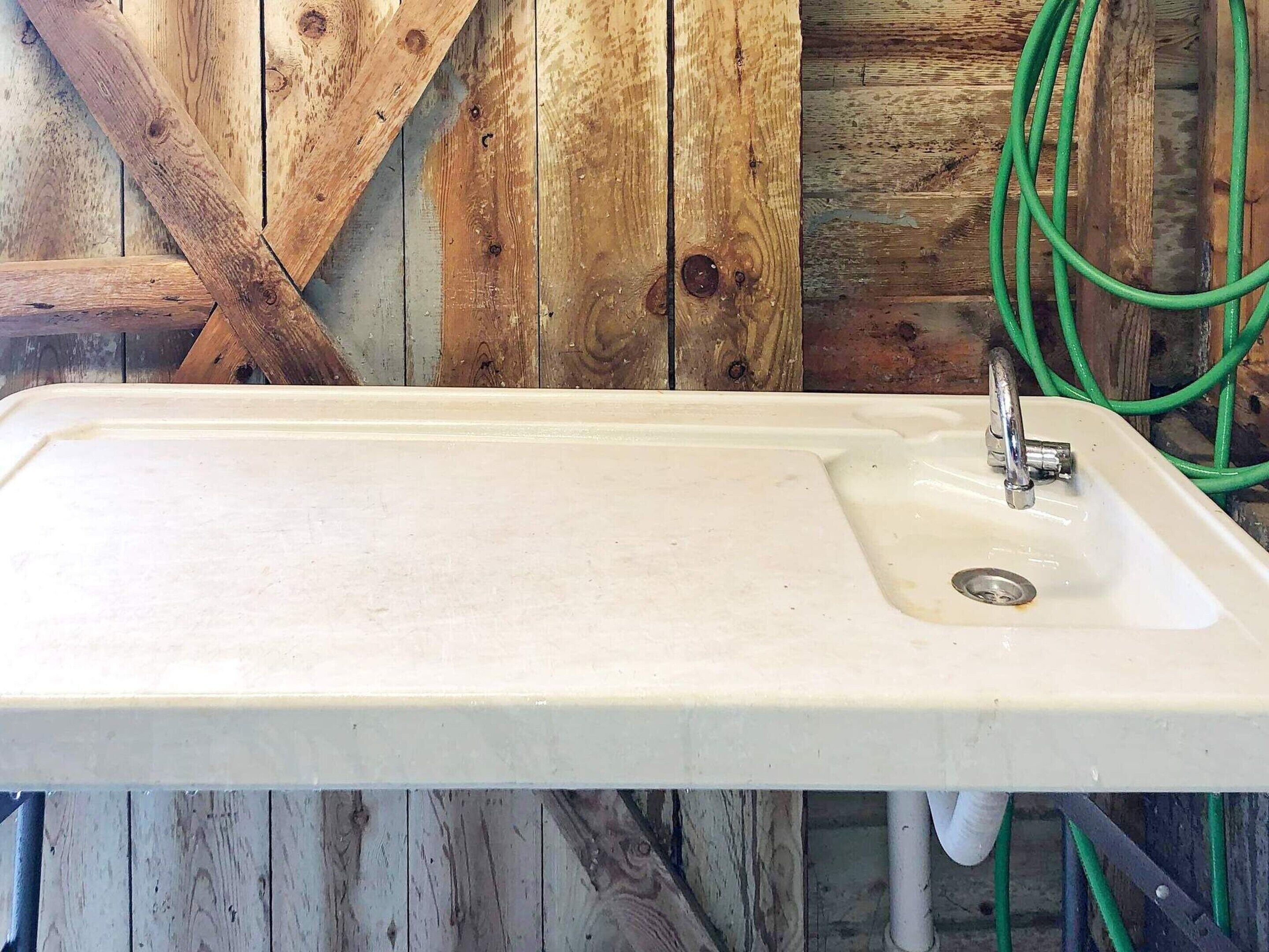 Un lavamanos rectangular blanco con un solo grifo, frente a una pared de madera rústica con veta y nudos visibles.