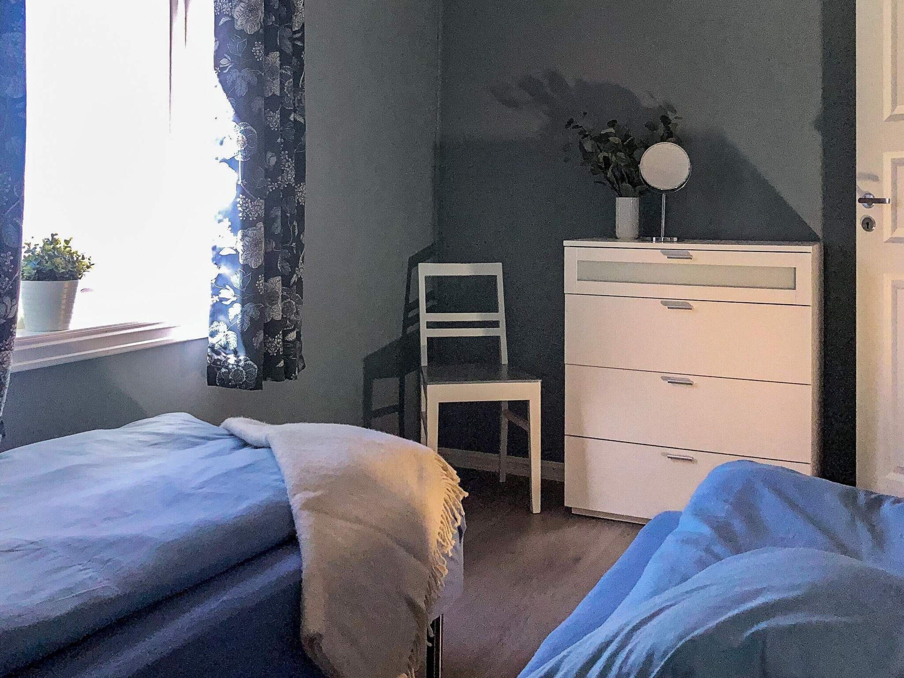 Een slaapkamer met twee bedden, een dressoir, een stoel en een raam met gordijnen.
