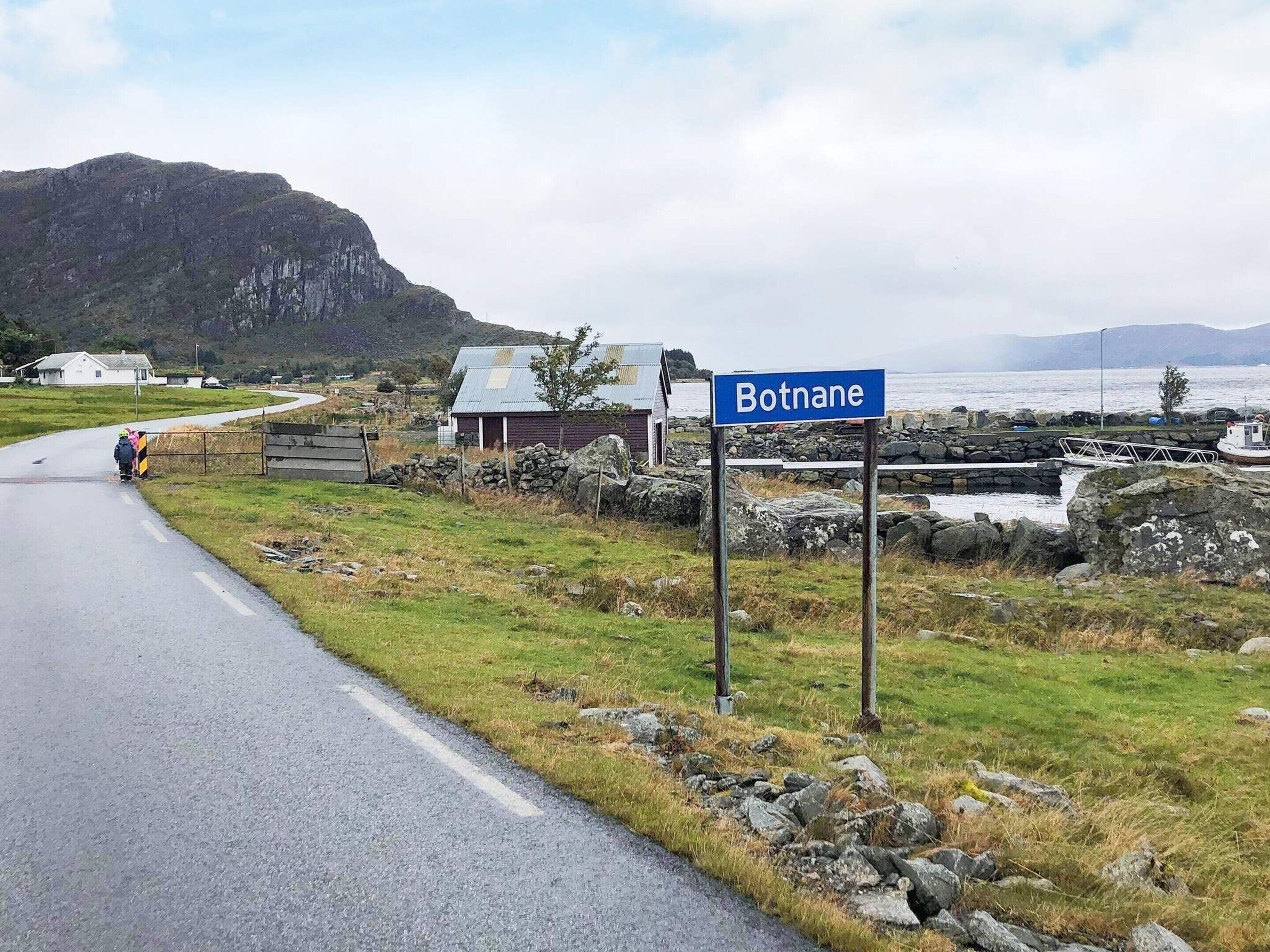 A rural road with a sign reading "Botnale" and a small building with a metal roof.