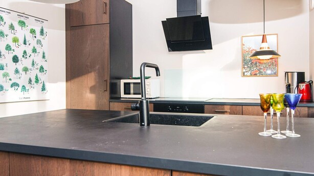 A modern kitchen with a black countertop, wooden cabinets, a stainless steel sink, a microwave, and a black range hood. - 4 Star Holiday Home in Ans By (Ans)